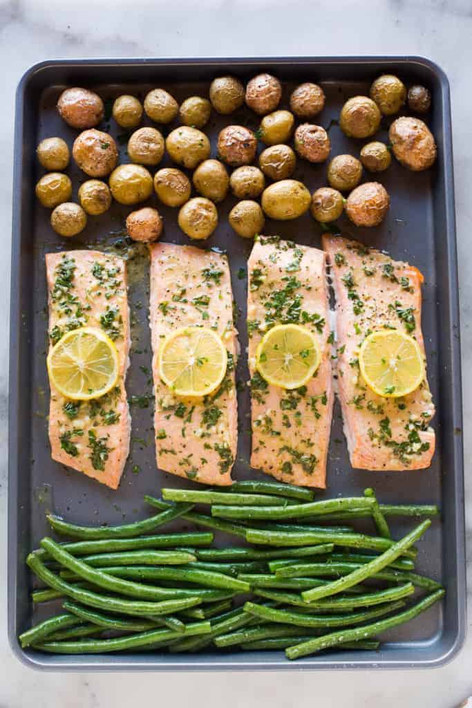 One pan baked salmon and vegetables on a large sheet pan with small red and yellow potatoes and green beans.