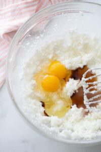 Eggs and vanilla added to a mixing bowl with creamed shortening and sugar.