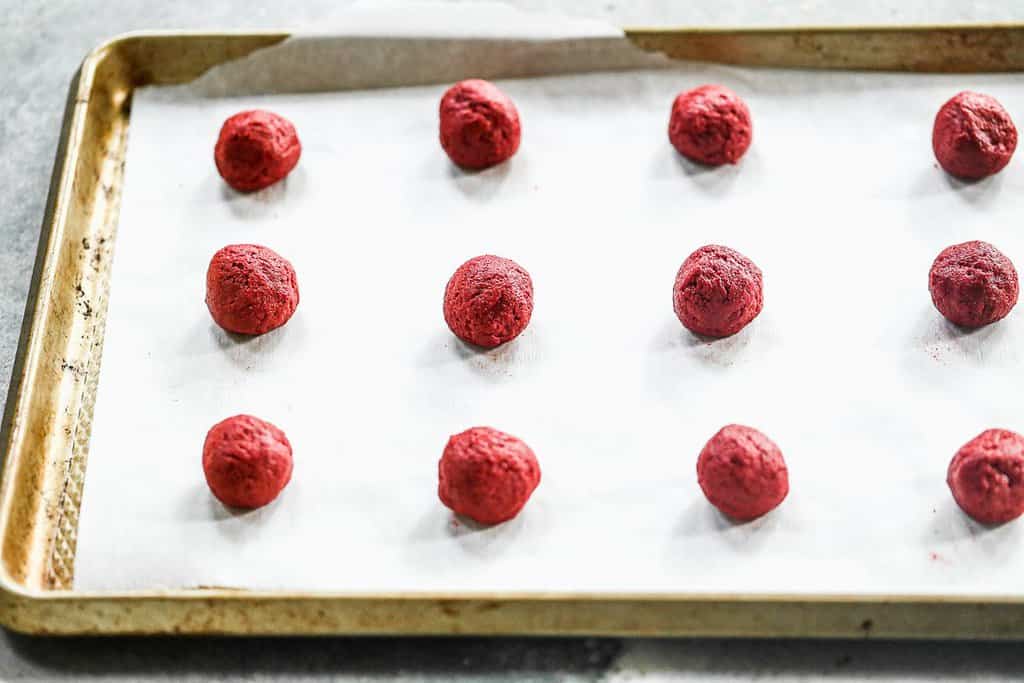 Red velvet cookie dough balls on a cookie sheet.