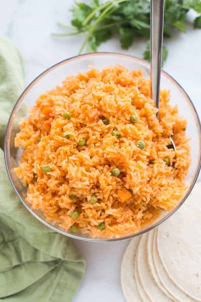Instant Pot Mexican Rice in a clear mixing bowl with a serving spoon and a green cloth on the side.
