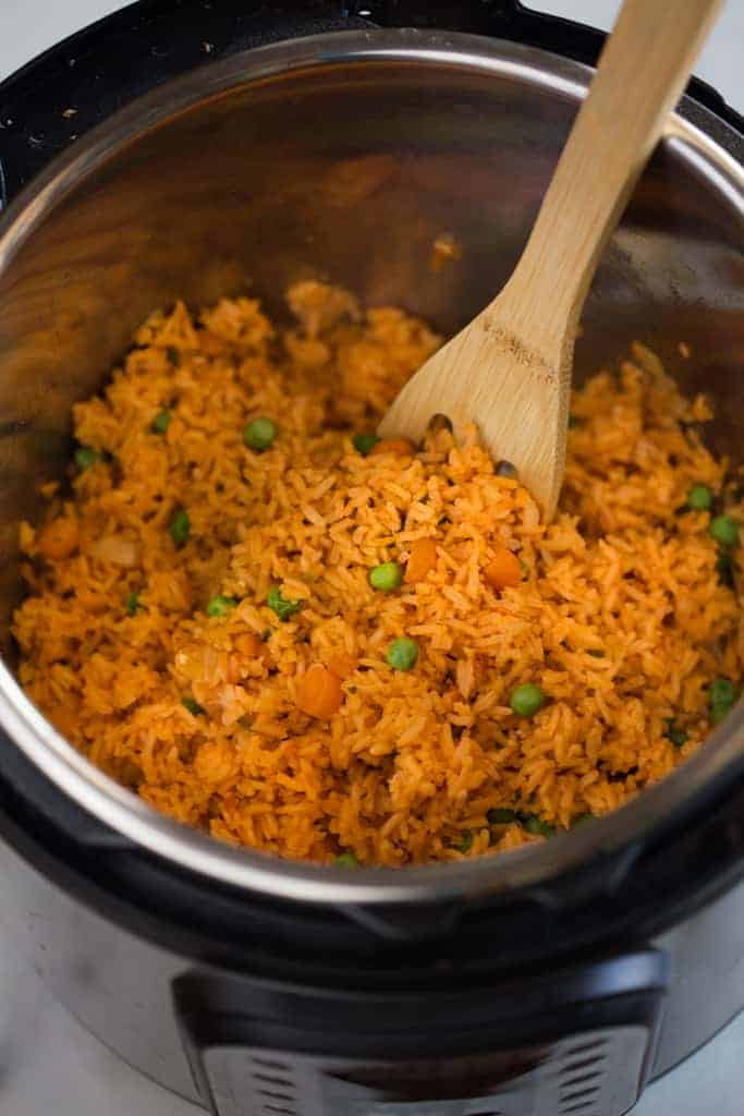 Cooked Mexican rice with peas and carrots, inside an instant pot, served with a wooden spoon.