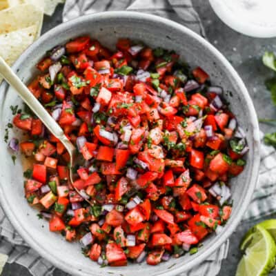 Pico de gallo served in a bowl, with a spoon, and chips on the side.
