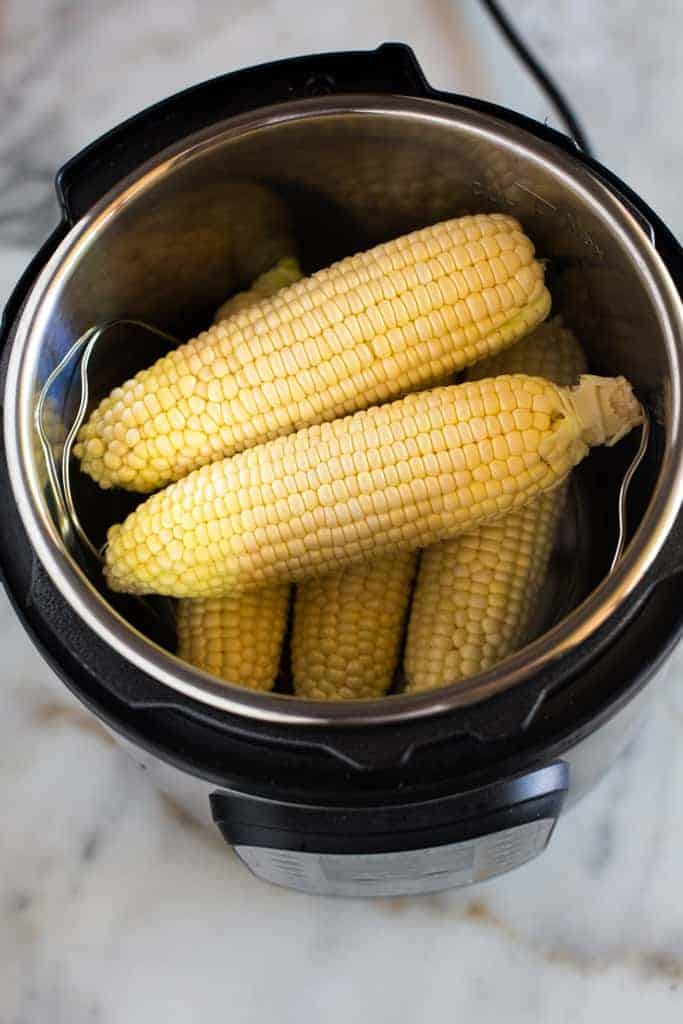 Raw ears of corn that have been husked and placed inside an instant pot.