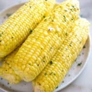 Perfect cooked ears of corn on the cob garnished with butter, salt and pepper and stacked on a white plate
