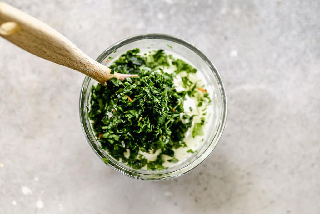Fresh cilantro being stirred into a jar of homemade creamy cilantro lime sauce.