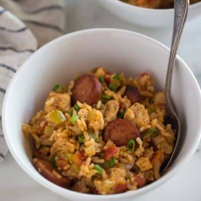 A white bowl full of jambalaya with chicken and sausages made in the instant pot, served with a spoon.