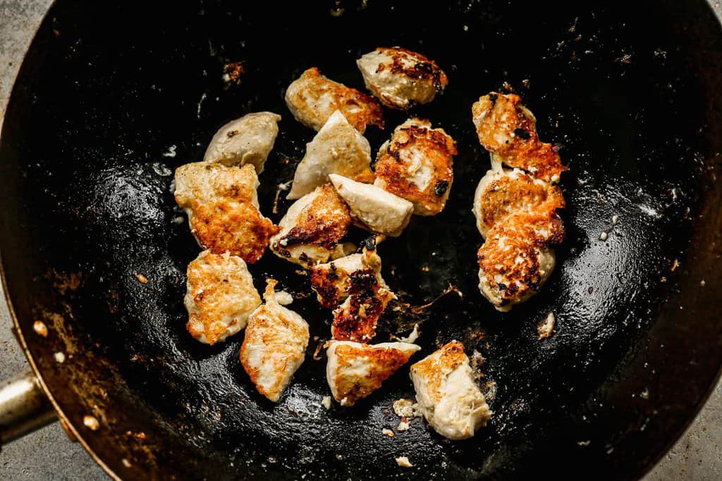 Marinated chicken pieces sautéing in a hot skillet.
