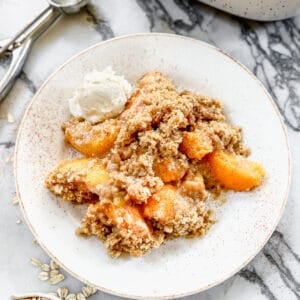 Fresh Peach Crisp topped with vanilla ice cream on a serving plate.