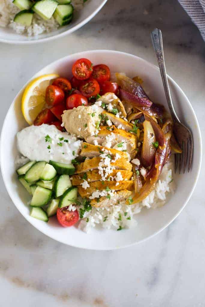 Chicken Shawarma bowls including a base of jasmine rice topped with marinated chicken, cucumber, tomato, red onion, hummus and tzatziki sauce.