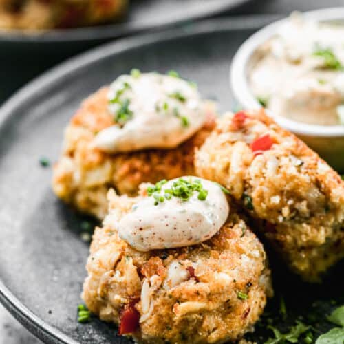 Three crab cakes on a plate with crab cakes sauce on top.