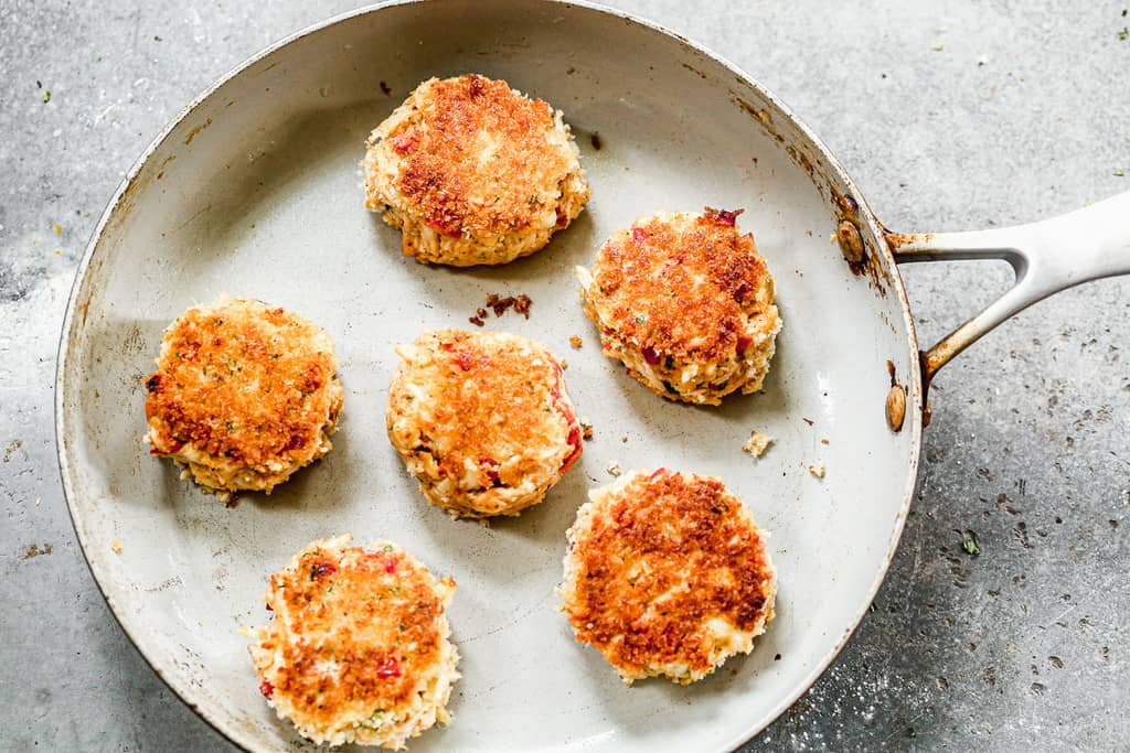 Six crab cake patties cooking in a skillet.
