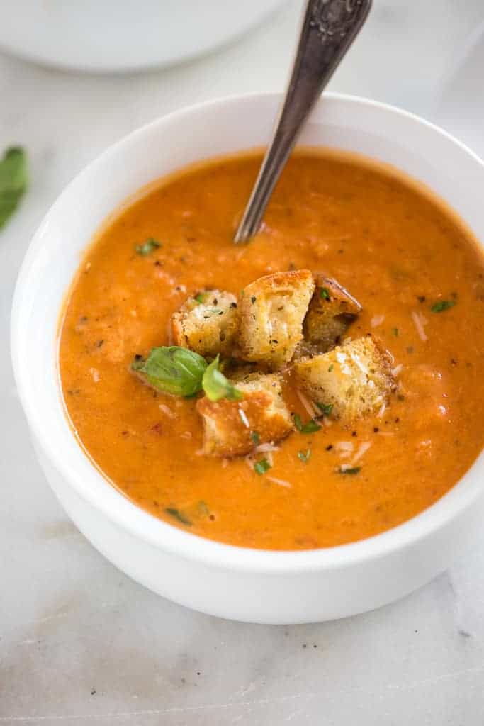Overhead photo of a white bowl filled with tomato basil soup with parmesan cheese, croutons, and a spoon.