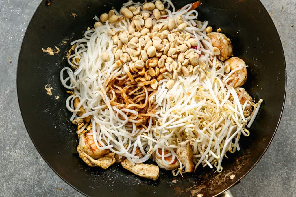 Nouilles pad thaï et sauce ajoutées à un wok avec légumes sautés, poulet et crevettes.