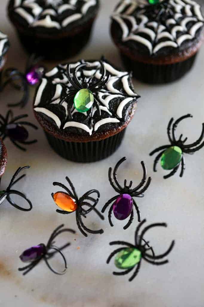Toy spider rings with colored jewels on top used to decorate the halloween cupcakes in the background.