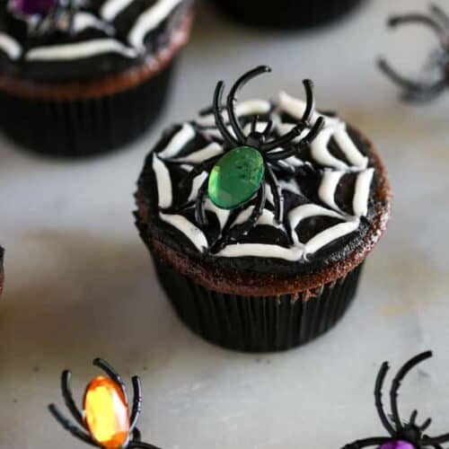 Halloween spider cookies made from a chocolate cupcake with black and white frosting to make a spider web, and a toy spider on top.