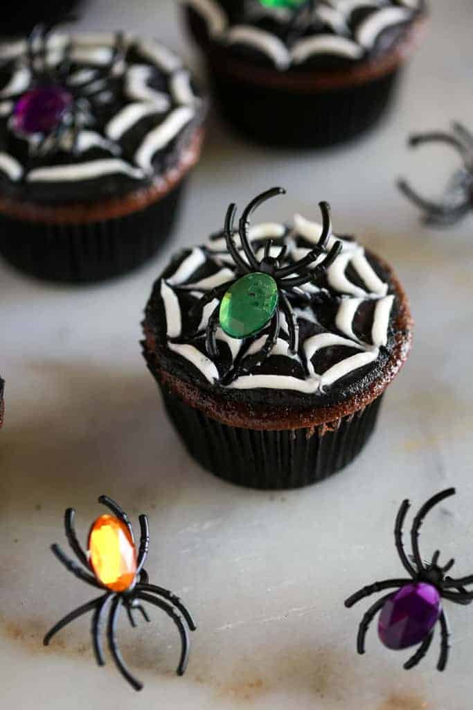 Halloween spider cookies made from a chocolate cupcake with black and white frosting to make a spider web, and a toy spider on top.