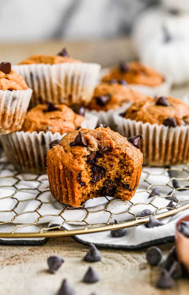 Healthy pumpkin muffins on a cooling rack, with a bite taken from one.