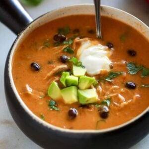 A bowl full of chicken enchilada soup that was made in the instant pot, topped with diced avocado, cilantro and a scoop of sour cream.