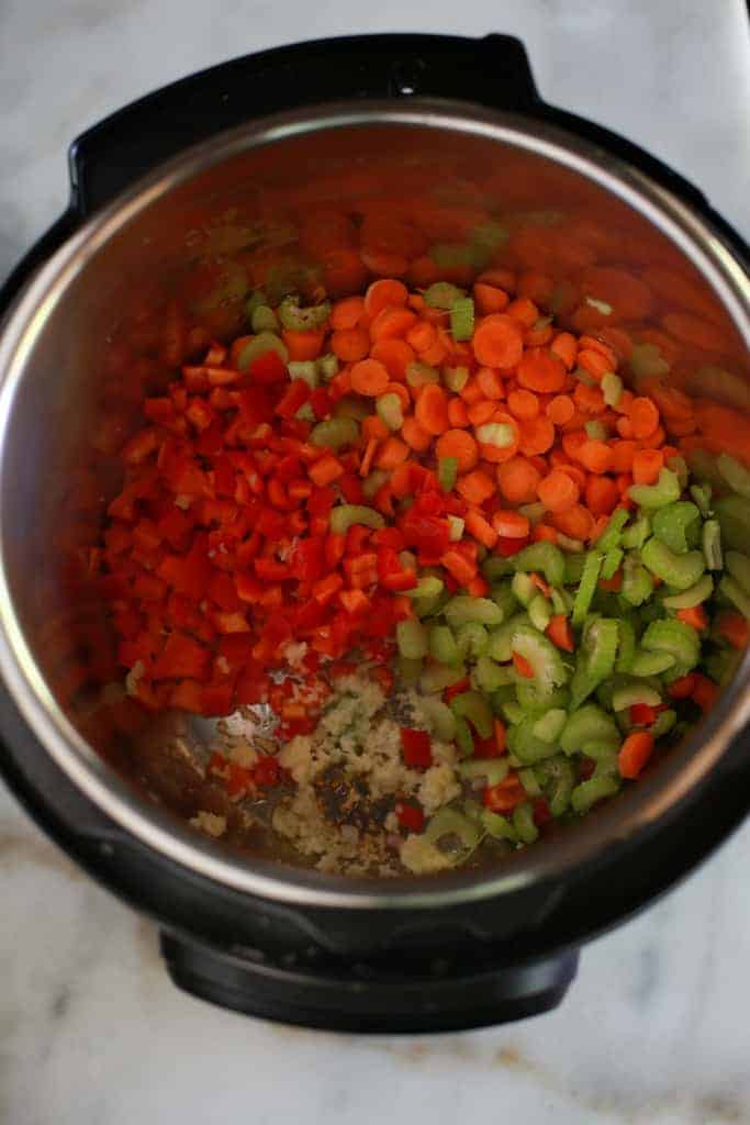 Vegetables sautéing in an instant pot including chopped carrots, bell pepper, celery, onion and garlic.