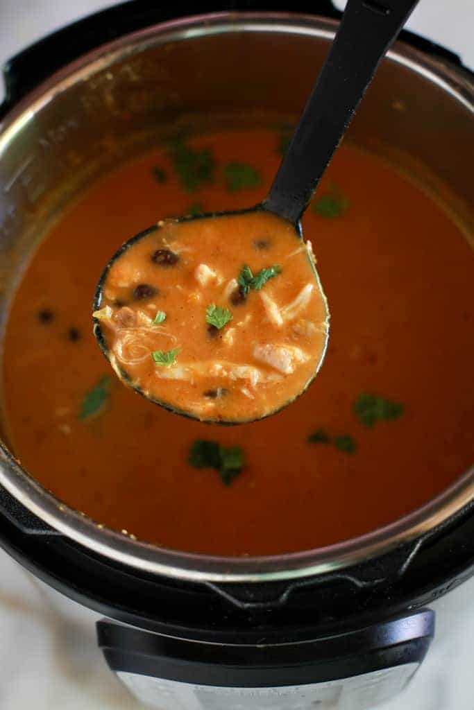 An instant pot filled with chicken enchilada soup and a ladle scooping some of the soup up.