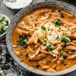 A bowl of Instant Pot Chicken Enchilada Soup topped with shredded cheese, green onions, adn sour cream.