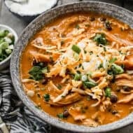 A bowl of Instant Pot Chicken Enchilada Soup topped with shredded cheese, green onions, adn sour cream.