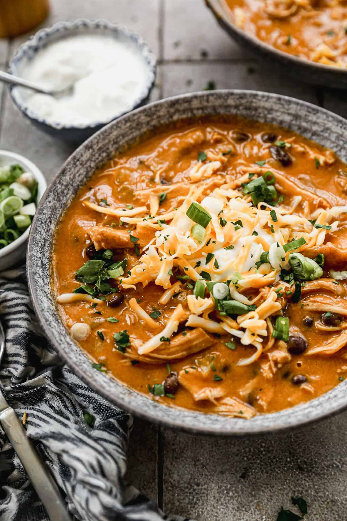 A bowl of Instant Pot Chicken Enchilada Soup topped with shredded cheese, green onions, adn sour cream.