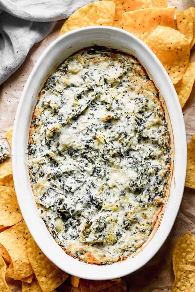 Overhead photo of a pan of hot spinach artichoke dip, surrounded by chips for dipping.