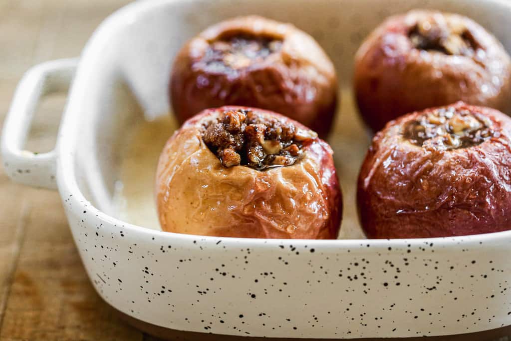 Four whole baked apples in a baking dish.