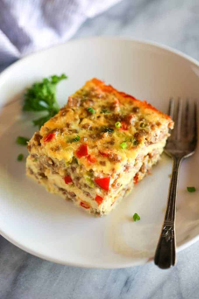 A slice of breakfast casserole on a white plate with a fork.