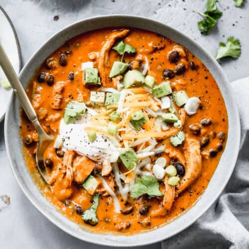 A bowl of chicken enchilada soup, served with sour cream, shredded cheese and chopped avocado on top.