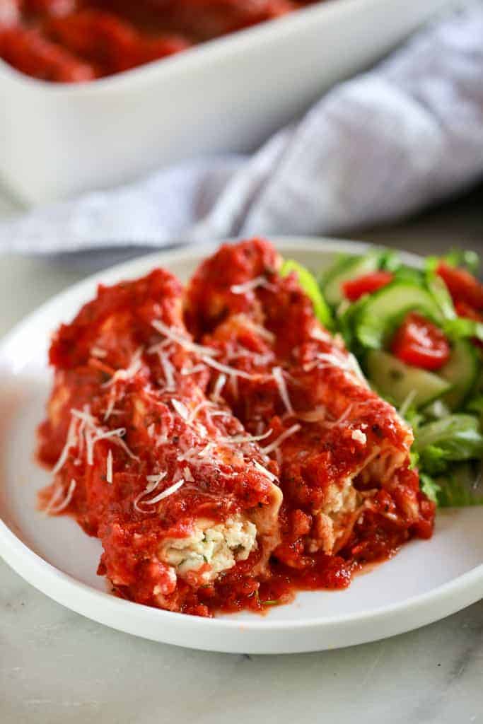Cheese manicotti with a homemade red sauce, served on a white plate with a side salad.