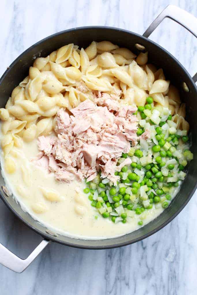 Overhead photo of a skillet with cooked medium shells noodles, tuna, a creamy white sauce and peas to make tuna noodle casserole.