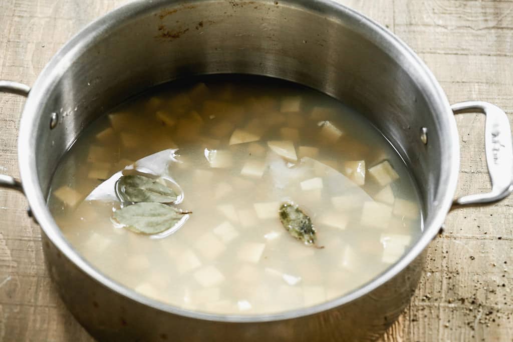 A soup pot with clam juice, broth, chopped potatoes and bay leaf.