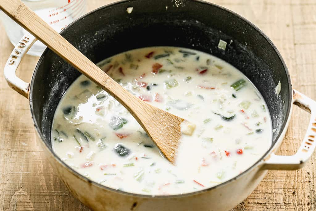 Clam chowder broth and sautéed veggies cooking in a pot.
