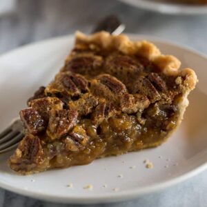 A slice of pecan pie on a white plate with a fork.