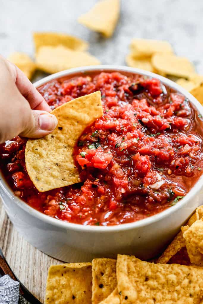 A bowl of easy homemade salsa with a tortilla chip being dipped in it. 