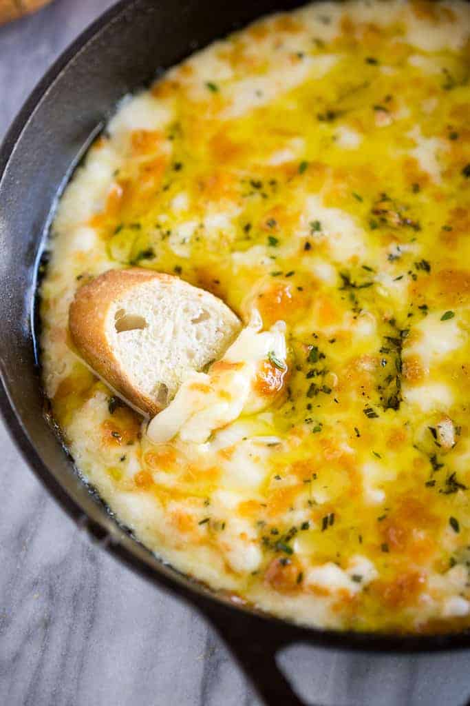 A small baguette slice nestled in a hot baked fontina cheese dip in a cast iron skillet.