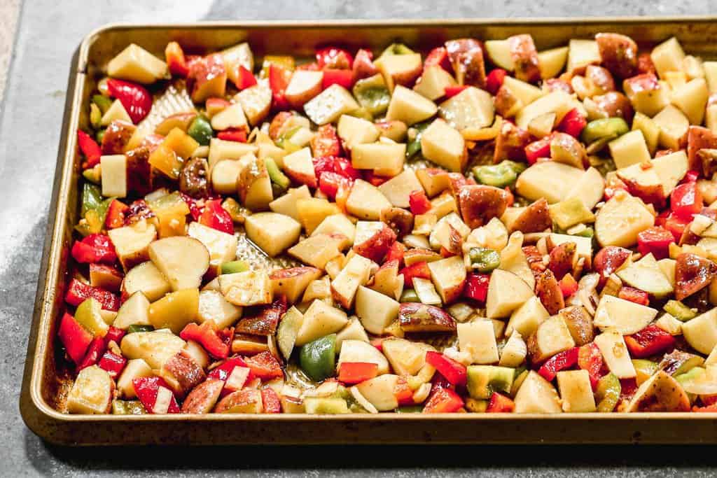 A sheet pan with chopped and seasoned potatoes and veggies to make oven breakfast potatoes.