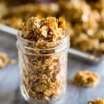 A mason jar filled with homemade granola and a sheet pan of baked granola in the background.