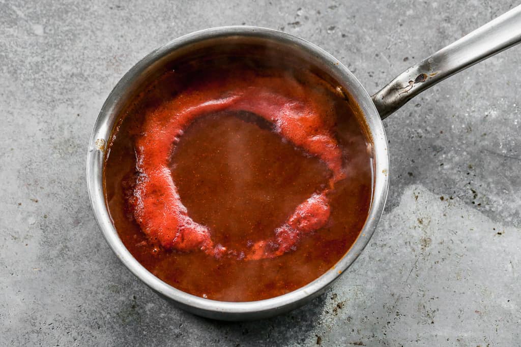 Sauce tomate et bouillon ajoutés à une casserole avec des épices et de la farine, pour faire une sauce enchilada.