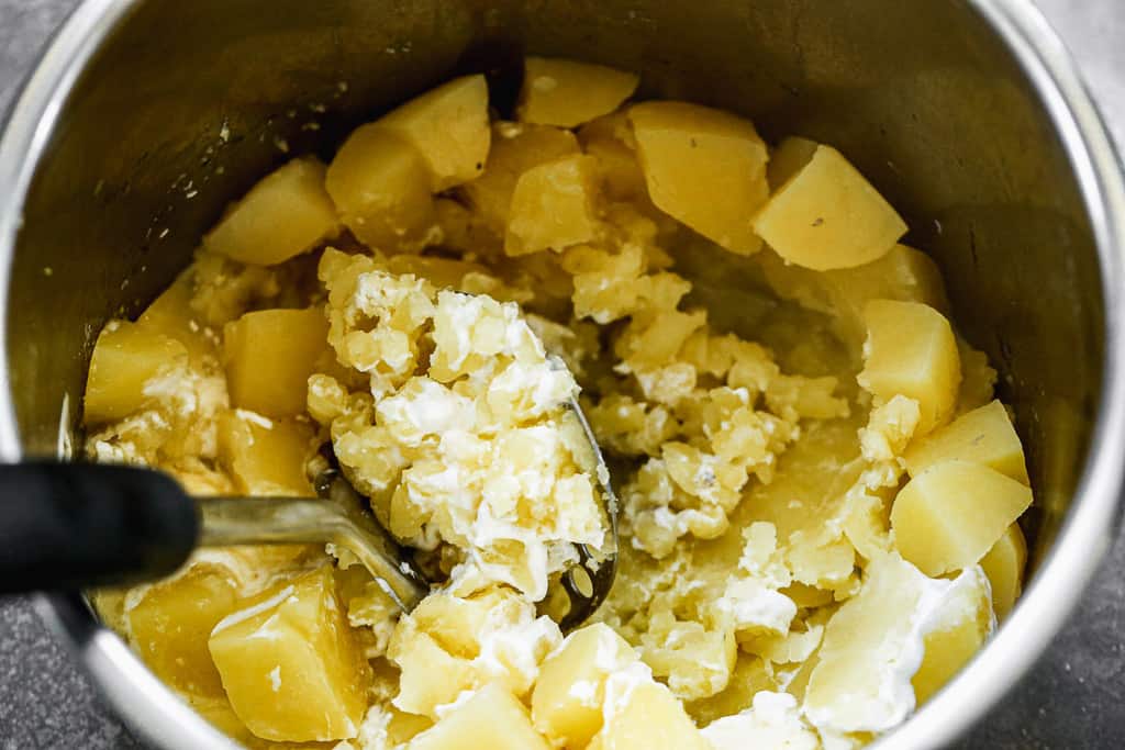 Penghancur kentang menumbuk kentang dalam panci instan.
