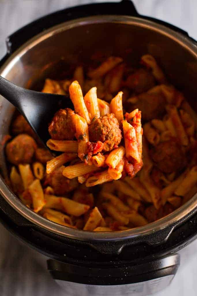 Overhead photo of an instant pot filled with penne pasta in a red sauce with meatballs, and a spoonful being lifted out.