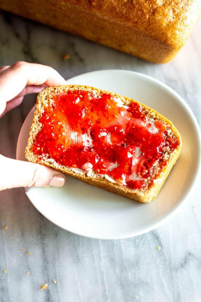 A slice iof homemade wheat bread with strawberry jam on top.