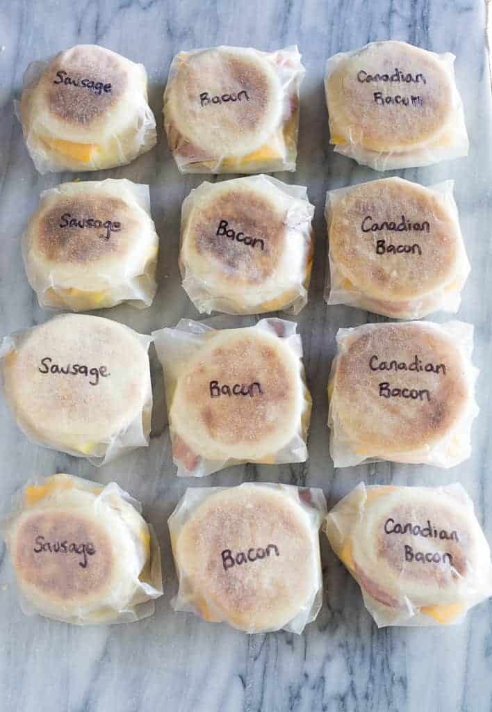 Twelve breakfast sandwiches wrapped in wax paper with the different names of the sandwich meat written on them.
