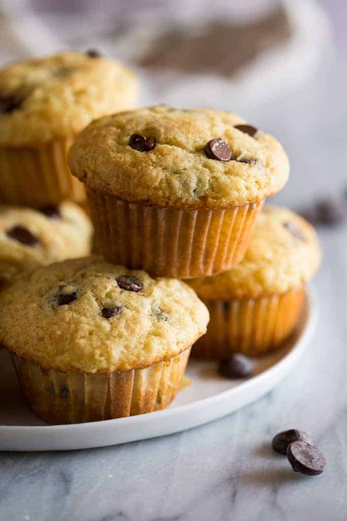 Chocolate chip muffins stacked on a white plate with chocolate chips in the background.