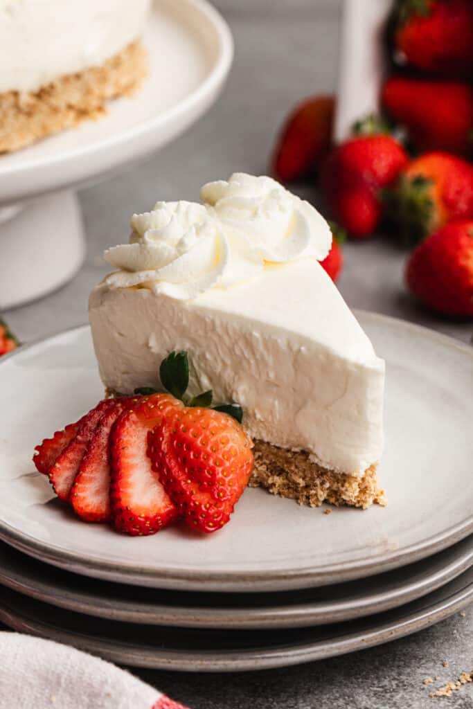 A slice of no bake cheesecake served on a plate, with a sliced strawberry.