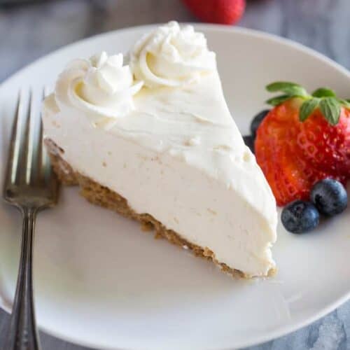 A slice of No-Bake Cheesecake on a white plate with a fork and berries on the side.
