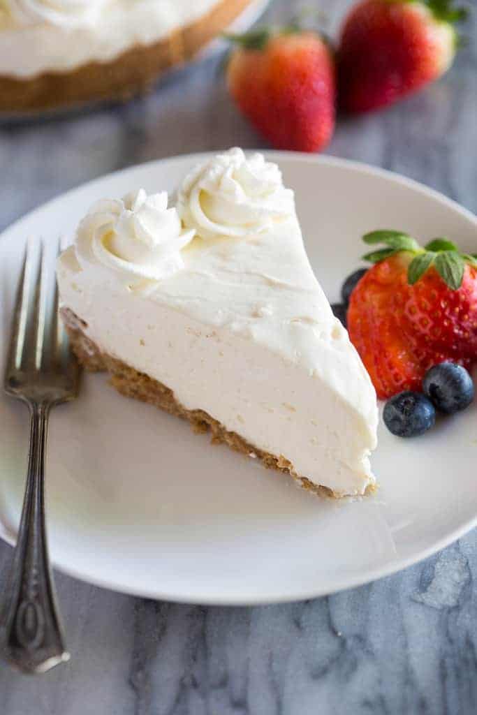 A slice of No-Bake Cheesecake on a white plate with a fork and berries on the side.