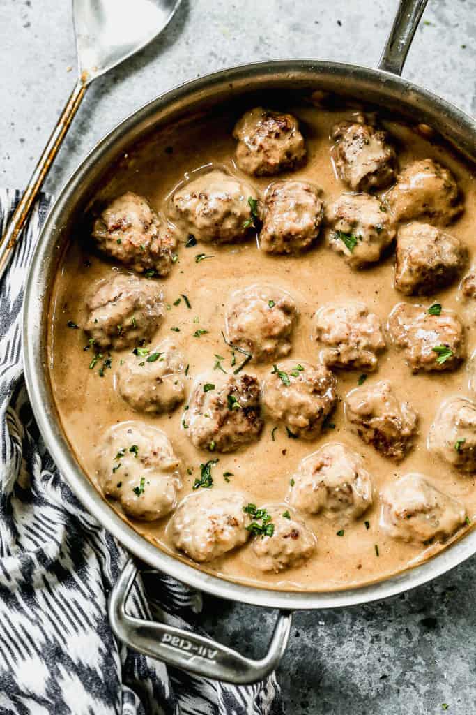 Swedish meatballs cooking in a skillet with gravy.